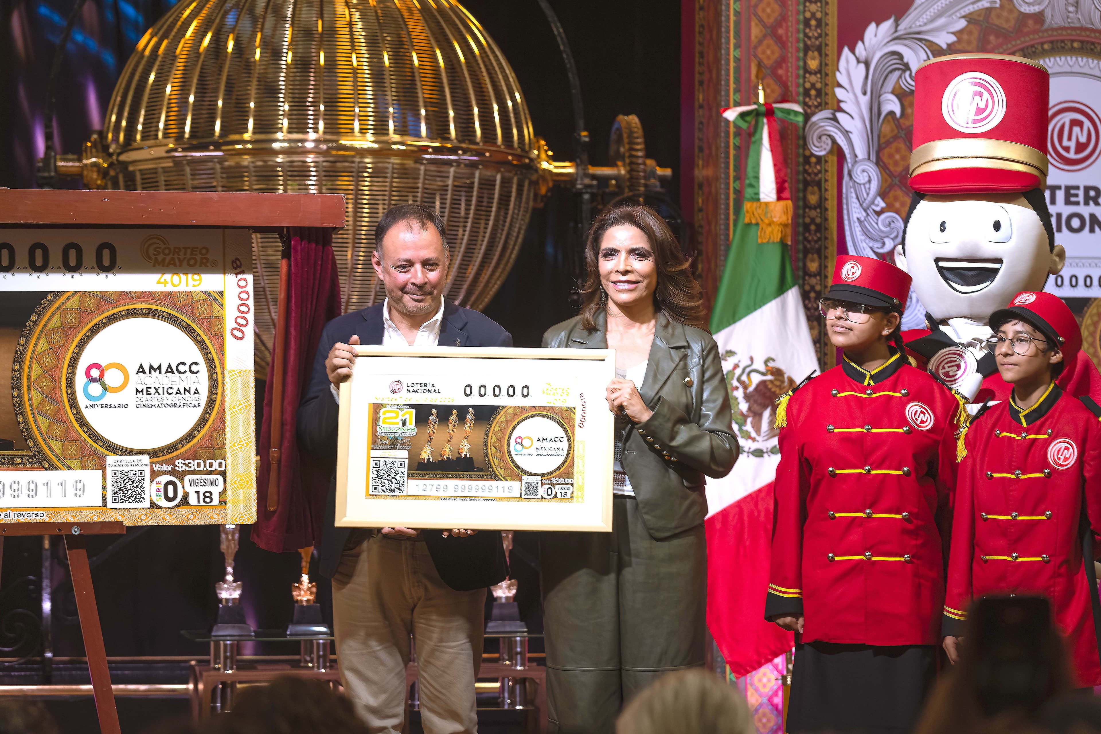 El presidente de la Academia Mexicana de Artes y Ciencias Cinematográficas (AMACC) y la directora general de la Loteria Nacional, XXX XXX, presentan el billete en honor a los 80 años de la academia.