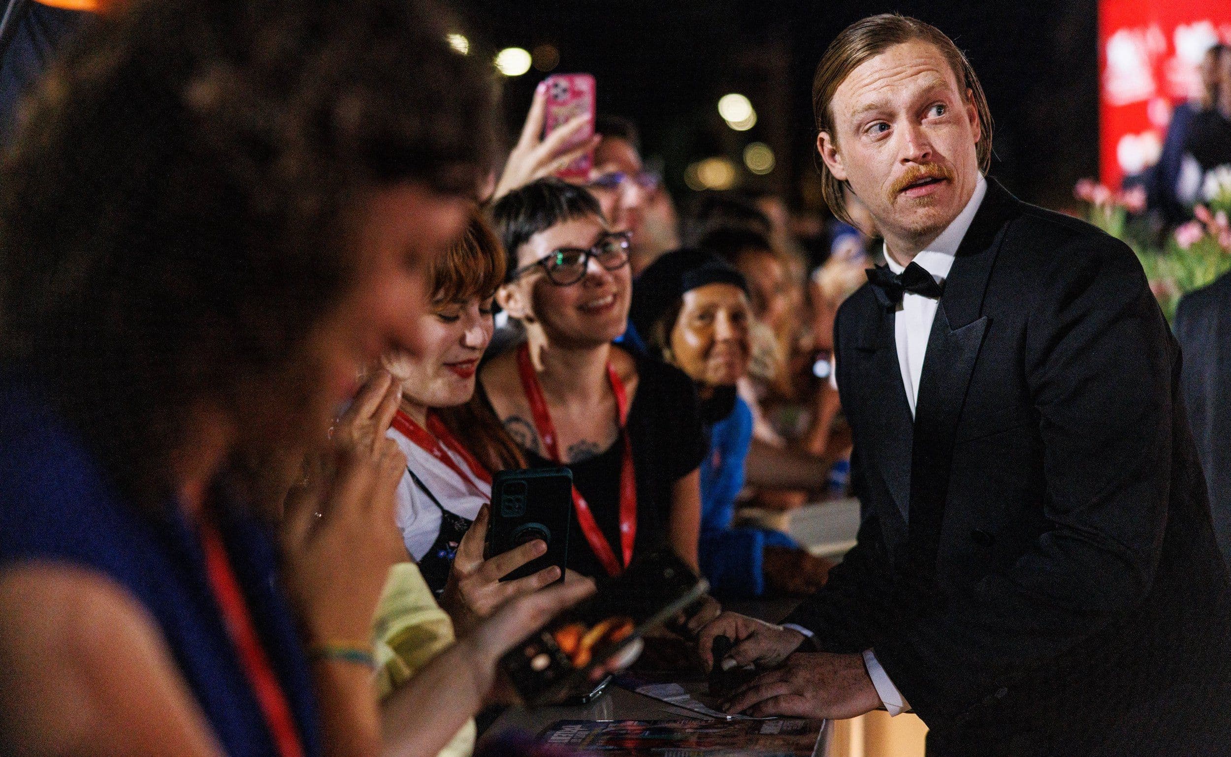 El actor Caleb Landry-Jones firma autógrafos en la alfombra roja de 'Dogman' durante la Mostra de Venecia